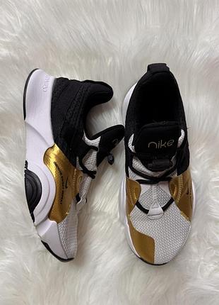 Жіночі кросівки nike superrep groove у біло-чорному дизайні з яскравим золотистим металевим акцентом на боковій частині