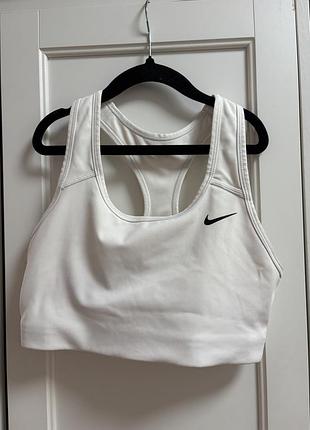 Білий жіночий спортивний топ (бра) від бренду nike із чорним фірмовим логотипом-галочкою (swoosh) з лівого боку.