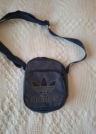 Сумочка adidas в темно-синьому кольорі в клітинку, є внутрішній карманчик і зовнішній на замку, шлейка регулюється