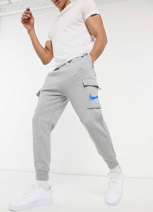 Серые спортивные штаны-карго nike с синим логотипом на кармане.