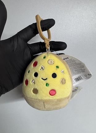 М'яка іграшка-кліпса squishmallows у вигляді шматочка піци на ім'я чеа (chea the pizza), яка має зручний пластиковий карабін для кріплення
