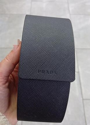 Жесткий черный футляр для очков бренда prada с характерной сафьяновой текстурой (saffiano) и тисненым логотипом на клапане
