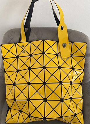 Жовта глянцева геометрична сумка-тоут у стилі bao bao issey miyake з характерними трикутними віниловими панелями регульованими чорно-жовтими ручками.