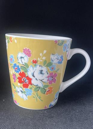 Жовта керамічна чашка бренdu cath kidston (серія stanley) з яскравим вінтажним квітковим принтом та білою ручкою.