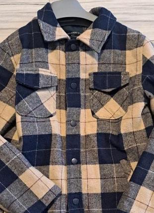 Теплая куртка-рубашка на парня 10-12 лет (overshirt / lumber jacket) в бежево-черную клетку с двумя нагрудными карманами с клапанами и воротником.