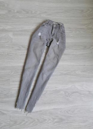 Сірі джинси з фабричними рваностями і необроботанным низом