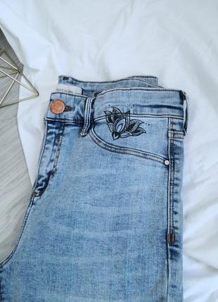 Винтажные голубые джинсы с фабричными рваностями и необроботанным низом с рисунками на высокой посадке на талию8 фото