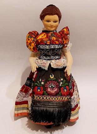 Старинная коллекционная кукла в национальной одежде, сидящая на стуле.