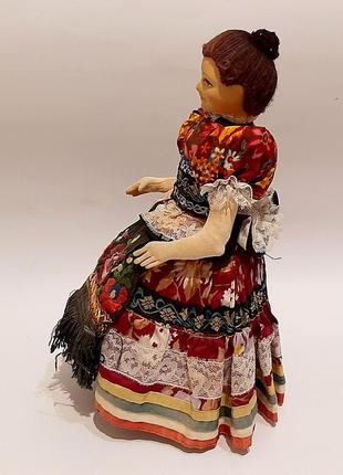 Старинная коллекционная кукла в национальной одежде, сидящая на стуле.4 фото