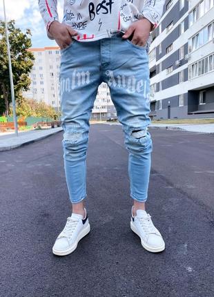 Мужские класичиские голубые  джинсы зауженые к низу с надписью потертостями и порезами на коленях2 фото