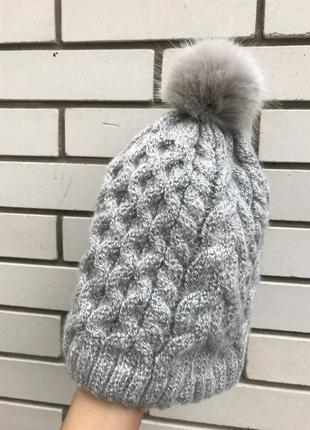 Тепла сіра в'язана в коси шапка з хутряним помпоном.